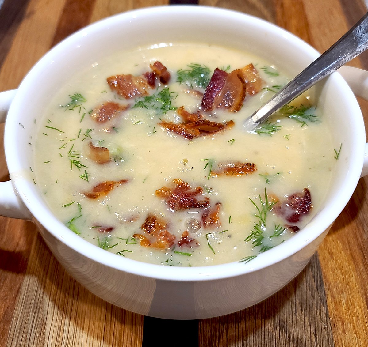 Potato Leek Dill Soup sprinkled with fresh dill and bacon in a white bowl