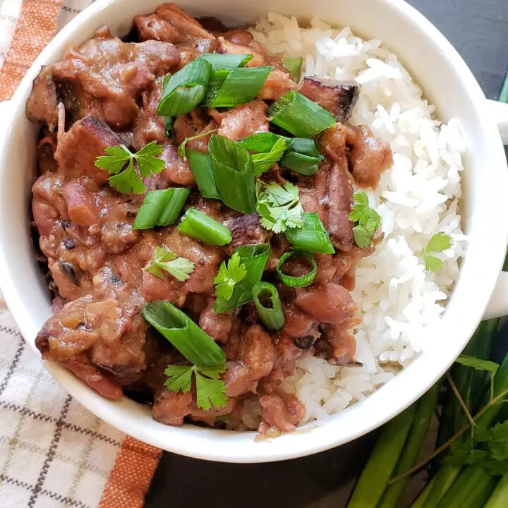 Red Beans and Rice with Diced Green onions on top in a white bowl on a black slate surface with a dish towl and green onions on the surface