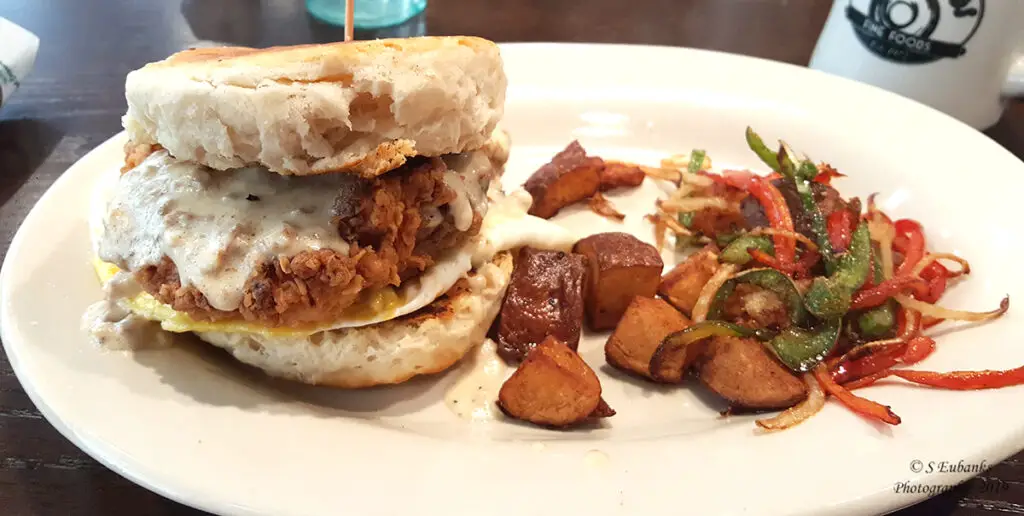 Chicken and biscuit sandwich on a white plate with homefries