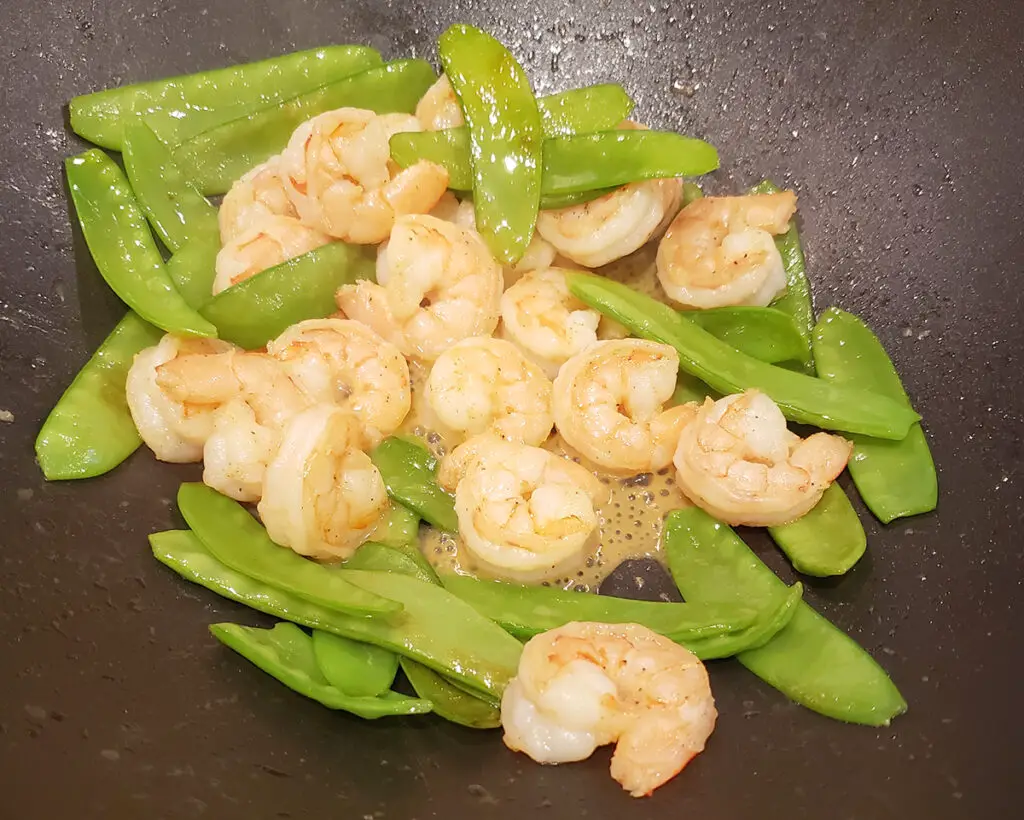 raw shrimp and snow peas in a wok