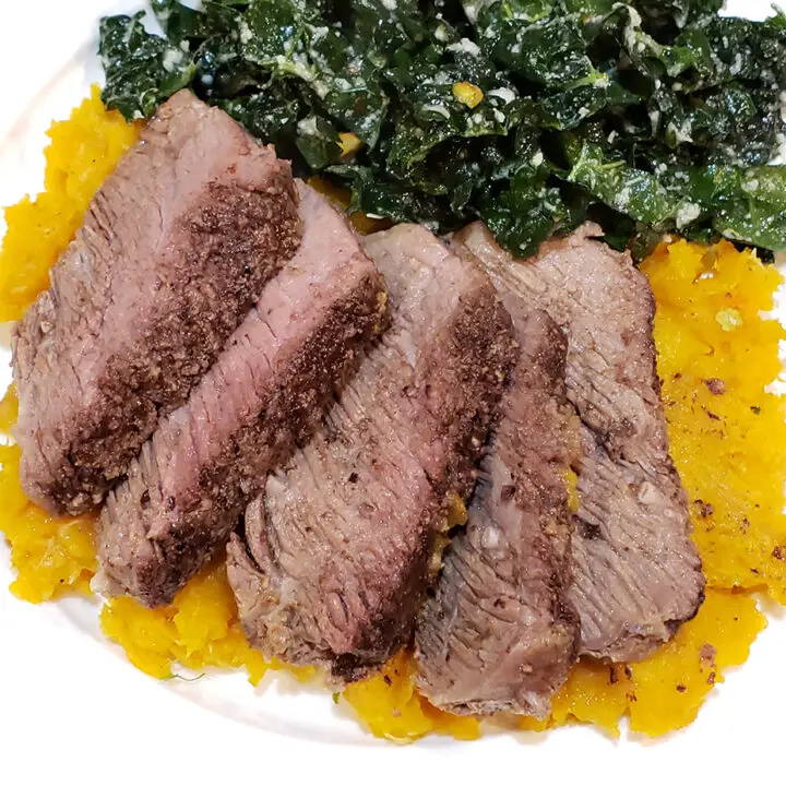 Slices of pot roast on a bed of butternut squash mash beside kale salad