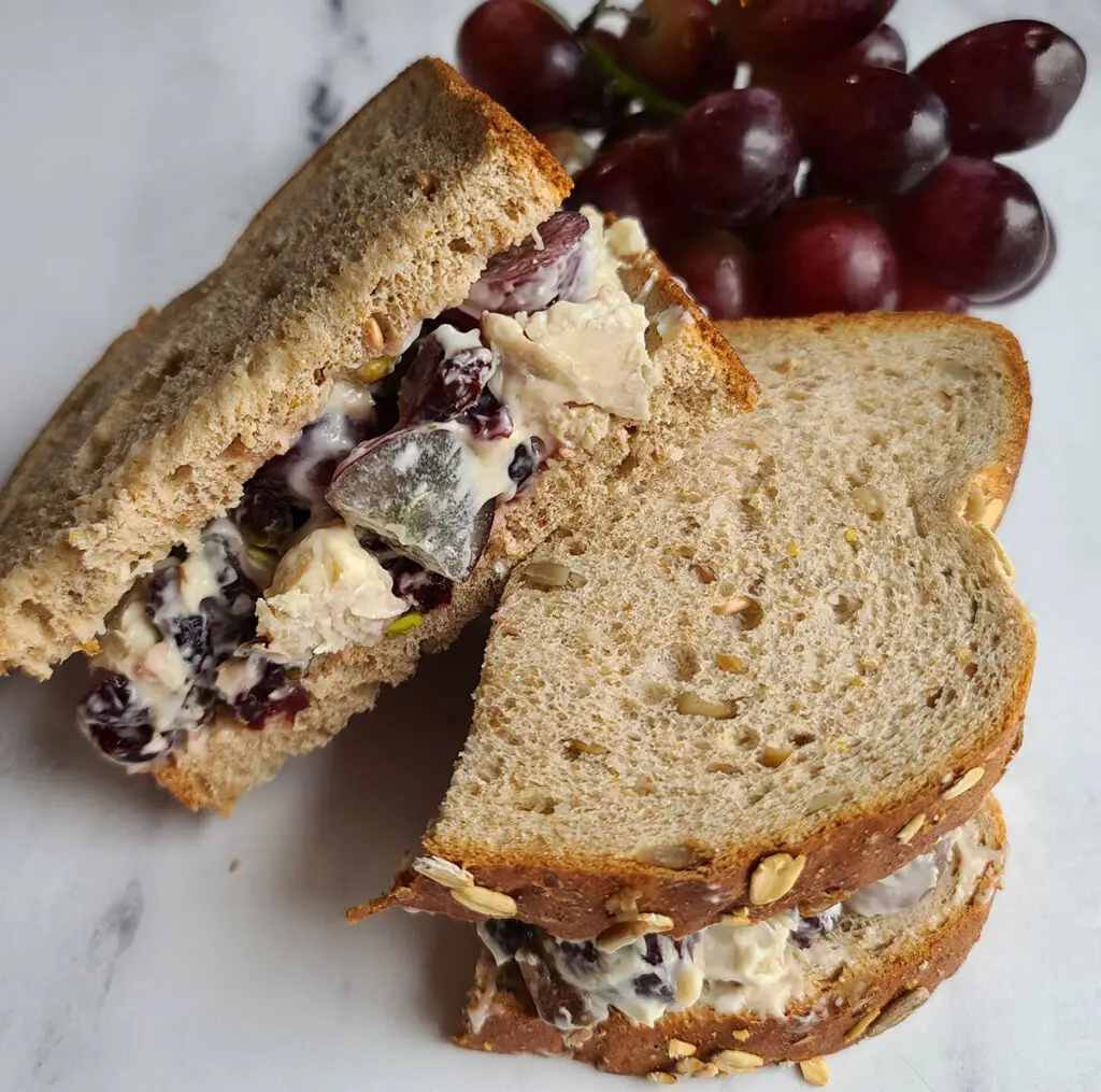 cranberry chicken salad sandwich halves with grapes in background