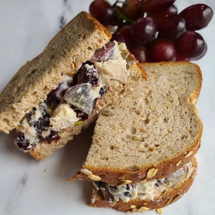 cranberry chicken salad sandwich halves with grapes in background