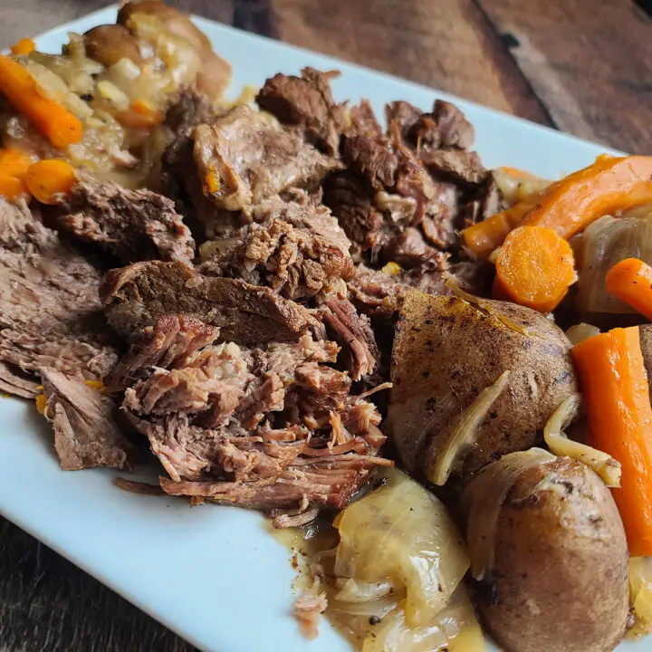 Shredded Instant Pot Pot Roast on a white plate with cooked potatoes, carrots and onions surrounding