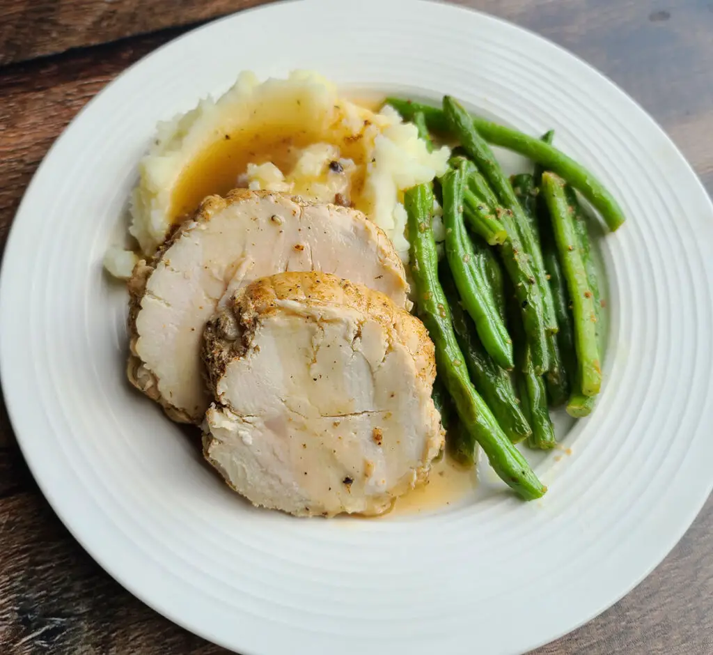 cajun seasoned turkey breast instant pot style. 2 slices piled on mashed potatoes with gravy poured over next to green beans on a white plate