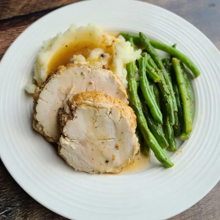 cajun seasoned turkey breast instant pot style. 2 slices piled on mashed potatoes with gravy poured over next to green beans on a white plate