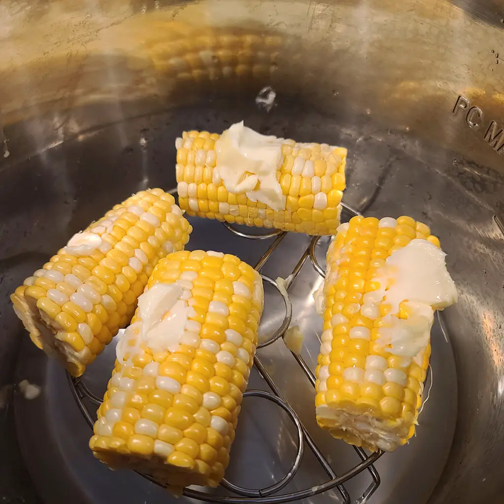 Four halves of Corn on the Cob with butter smothered on top.  Corn in on a metal rack in an instant pot.