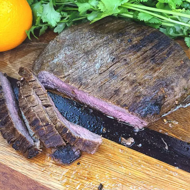 Carne Asada Steak sliced on a wood cutting board with cilantro and an orange in the background