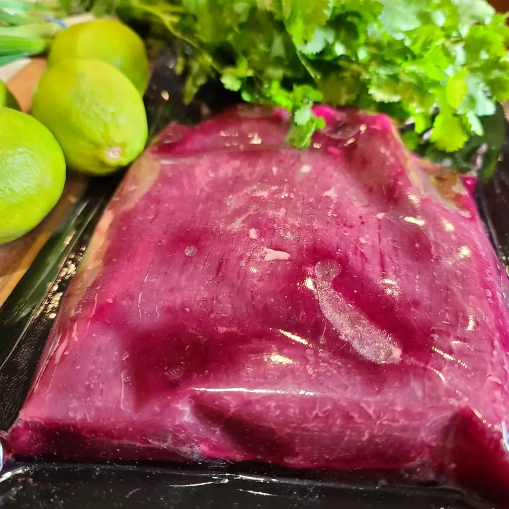 Vacuum packed Flank Steak meat surrounded by cilantro and limes