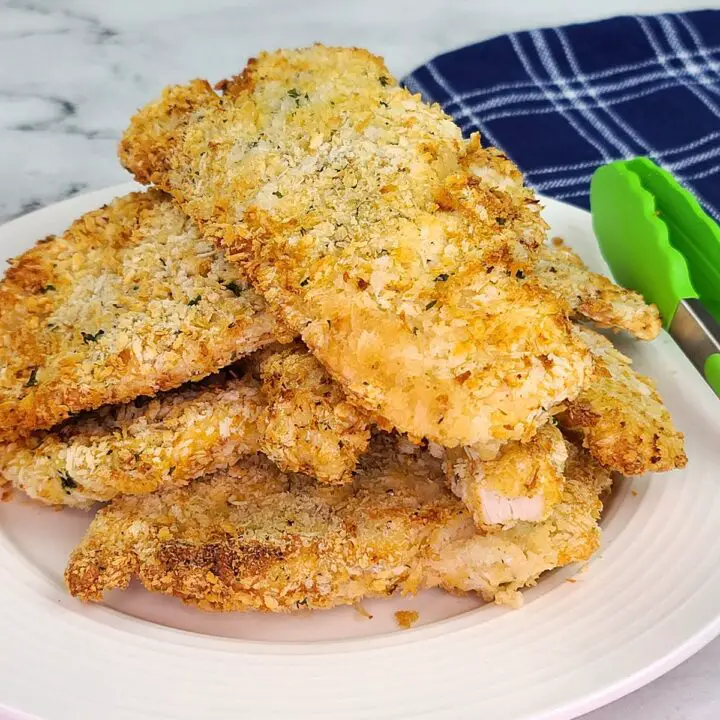 A stack of Air Fryer Chicken Cutlets on a white plate. Green tongs resting on the side of the plate next to a blue and white dish towel.